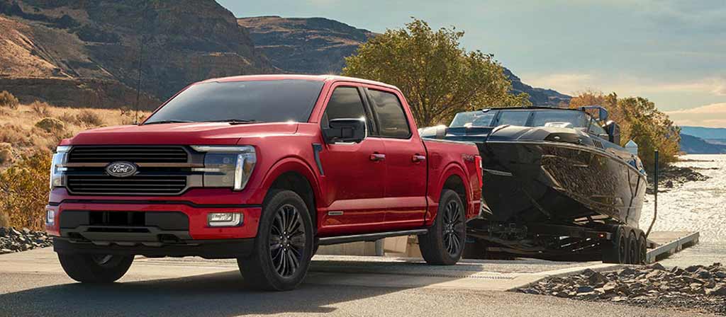 Ford F-150® roja remolcando una lancha negra en una rampa frente al agua con montañas de fondo