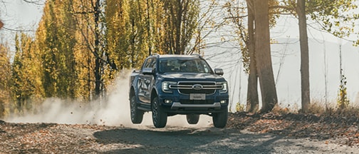 Ranger azul avanzando por sendero arbolado con luces frontales encendidas